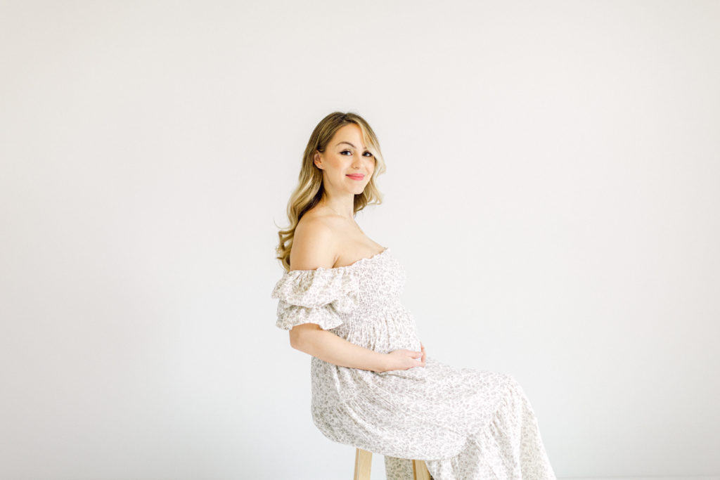 Pregnant woman sitting on a stool in a floral dress during her maternity session