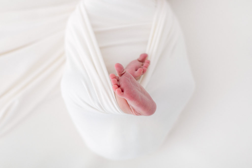 Newborn baby swaddled in white blanket with feet showing