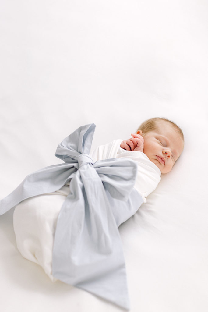 Newborn baby boy swaddled in white blanket and blue bow taken by Hyde Park Newborn Photographer