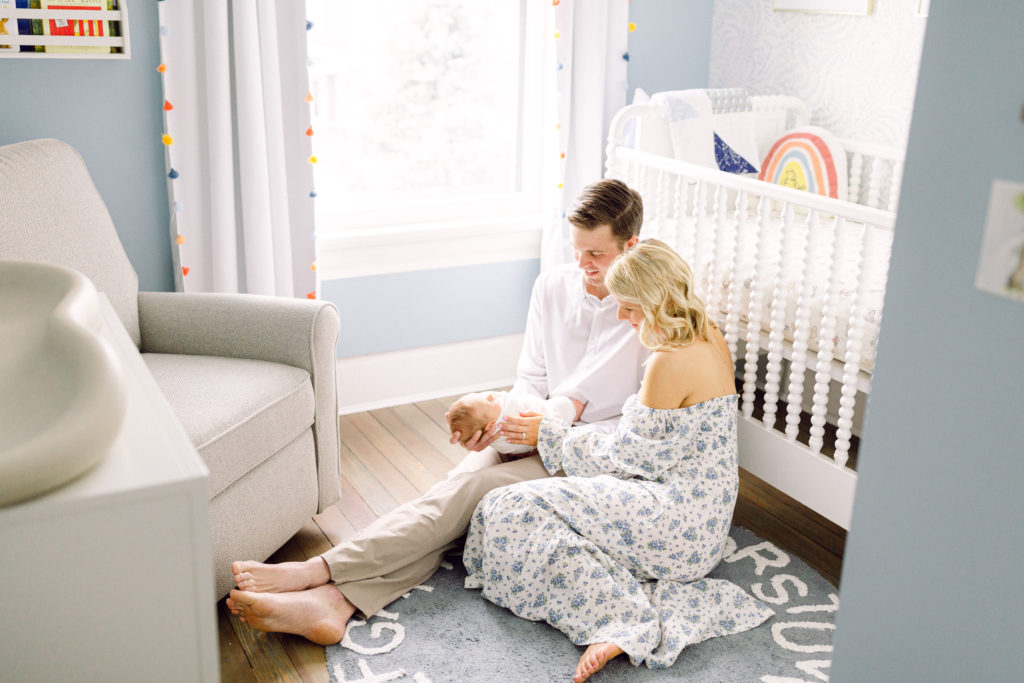 Mother and father sitting on the floor of nursery next to a white crib holding their newborn baby in their lap, taken by Hyde Park Newborn Photographer
