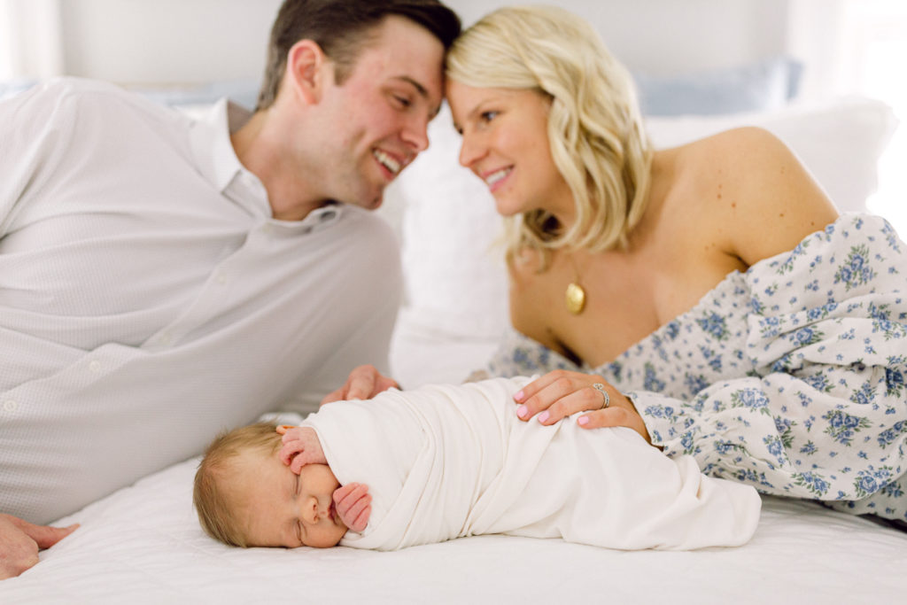 Mother and father laying on their bed next to their swaddled newborn son taken by Hyde Park Newborn Photographer