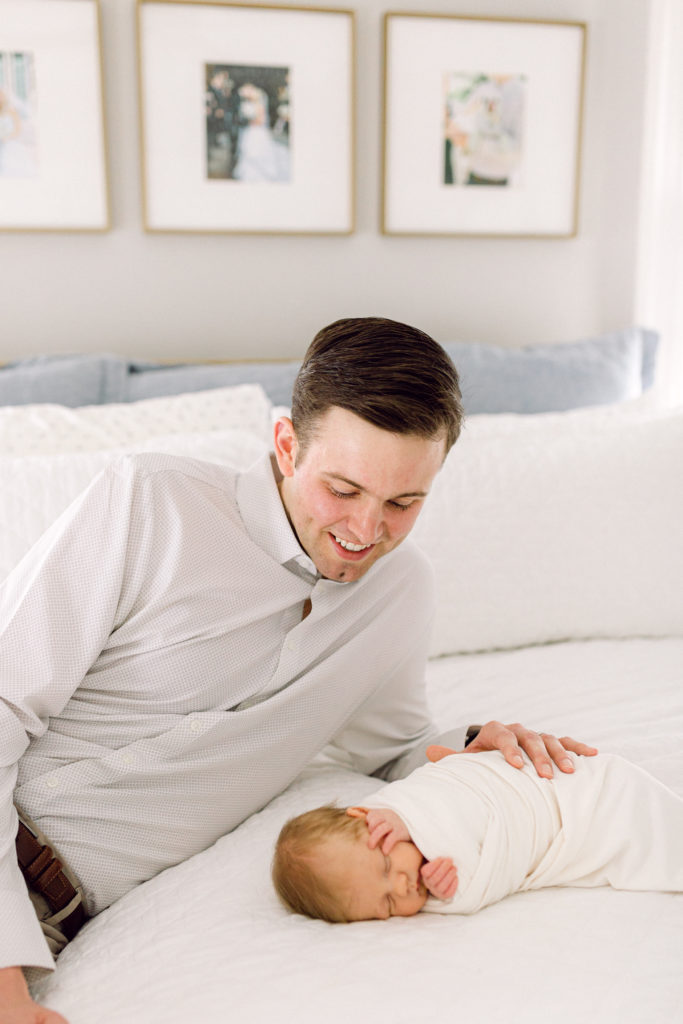 Father laying on his bed next to his swaddled newborn son taken by Hyde Park Newborn Photographer